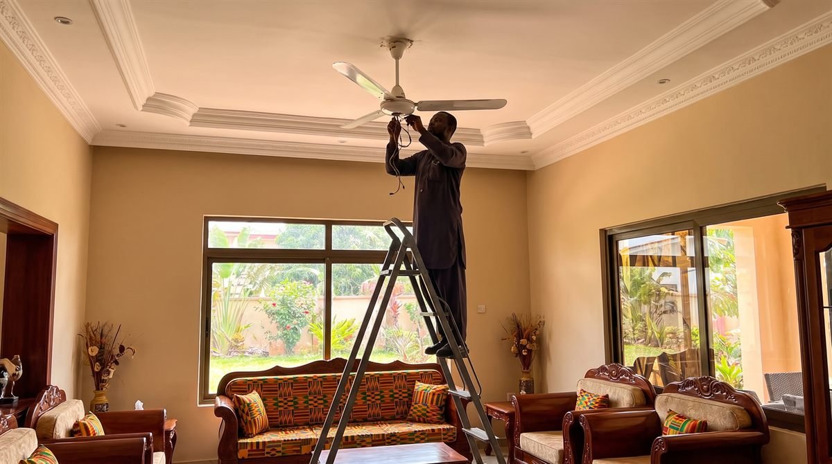 Technician on a ladder installing a ceiling fan in a living room decorated with Kente-pattern furnishings