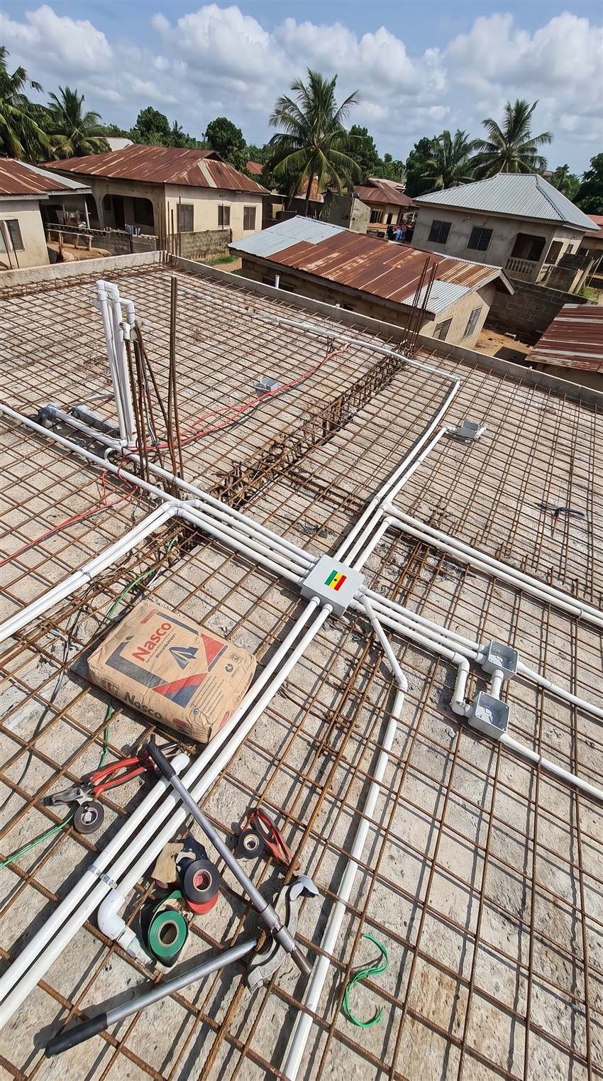 Pre-slab electrical conduit installation on a rooftop under construction in Accra, marked with the Ghana flag